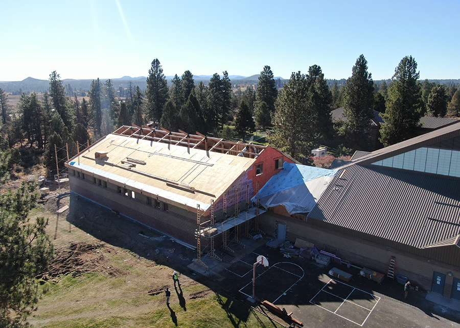 An ariel construction photo - trusses are in place, the roof has been paritially added, the Gym is coming together